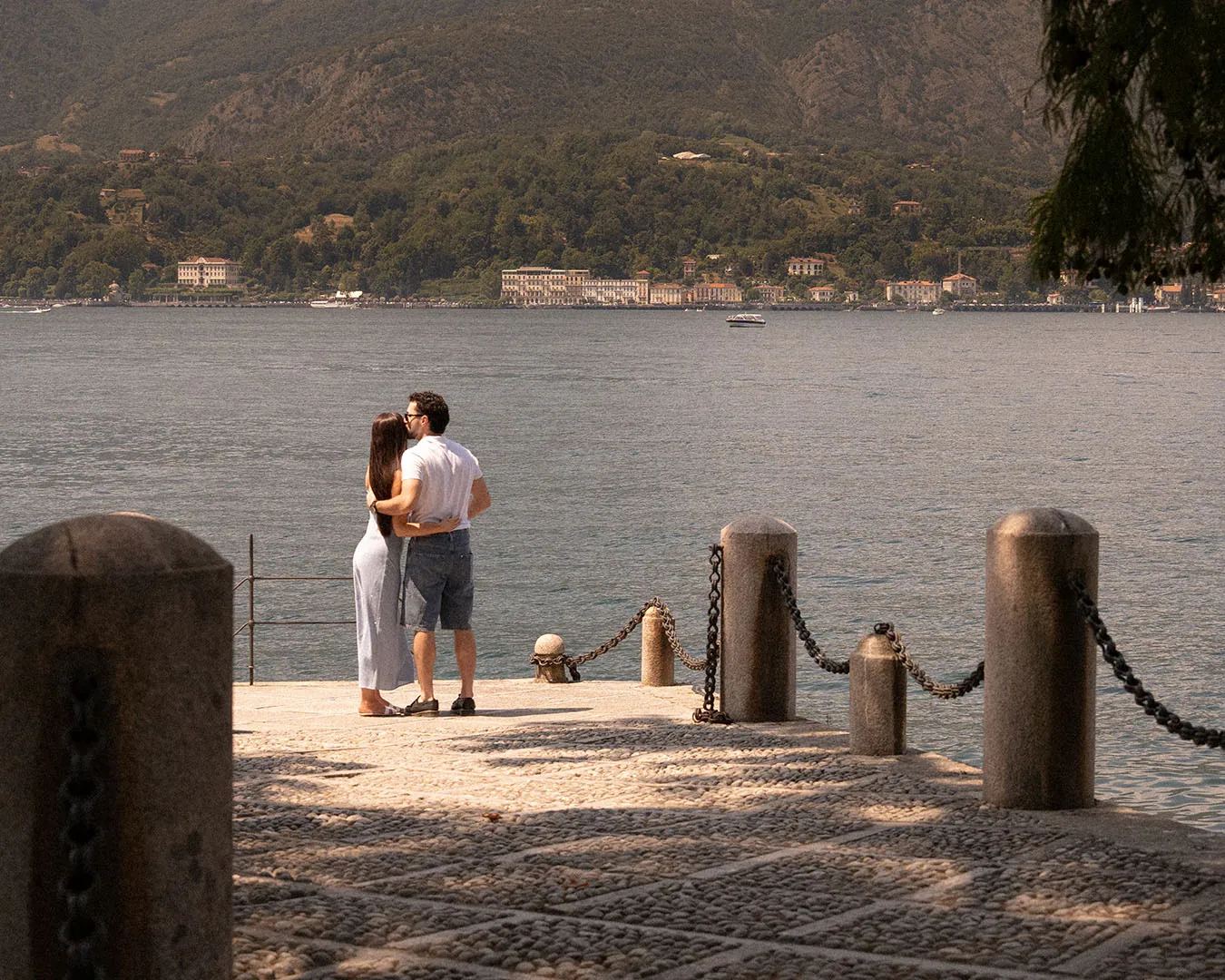 Winona and Valerio embracing on a stone pier on Lake Como, villas on the far shore